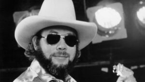 A man with a beard wearing sunglasses and a cowboy.