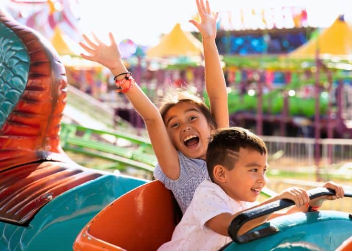 Two excited children with their arms raised on a carnival ride