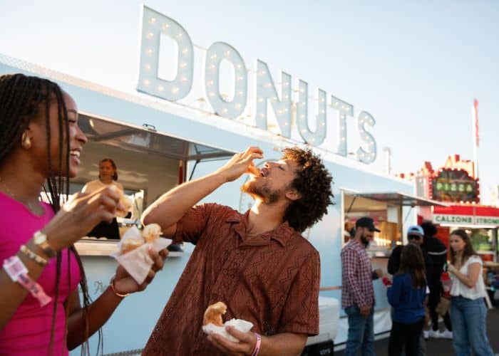 Two friends enjoying donuts in front of a food truck at the fair